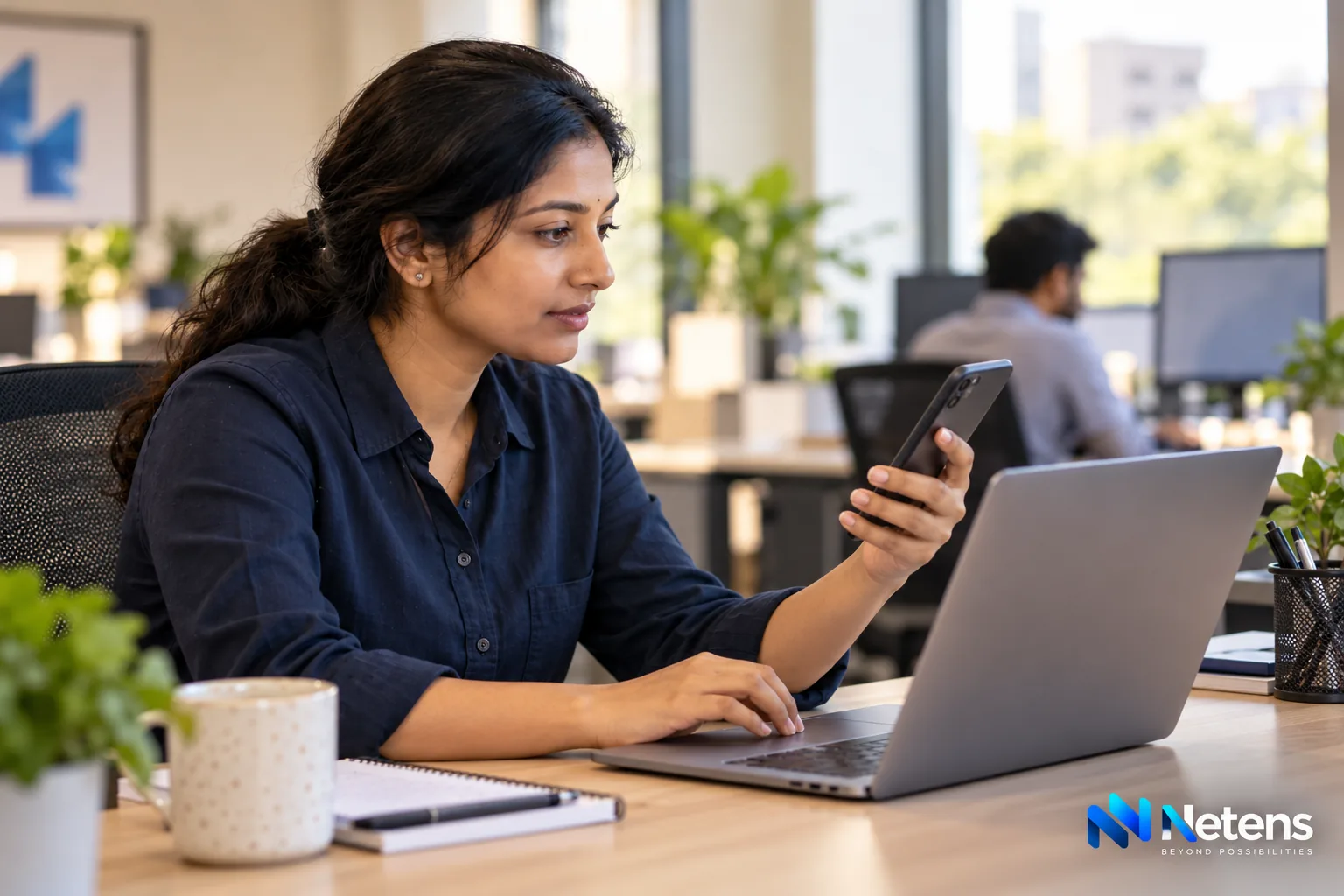 Indian web engineer checking a website on a smartphone beside her laptop
